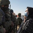 Palestinian woman wearing surgical mask faces an armed Israeli soldier
