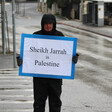 A person wearing a winter coat holds a sign in the street 