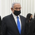 Netanyahu is seen from the waist up while wearing a mask inside a courtroom
