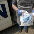 Man seen from chest down holds bag of UNRWA food aid in front of UN vehicle