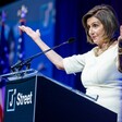 A woman stands at podium with arms outstreched