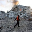 A man in an orange vest walks past the rubble of a building