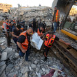 Men in emergency worker vests carry shrouded body away from destroyed building