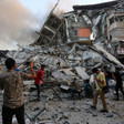 People stand by a pile of grey rubble from destroyed building 