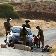 Four soldiers detain youths lying on the street next to a car