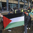 Two men hold flag, surrounded by a group of other people 