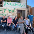 Seven men sit in front of a graffitied building, near rubble