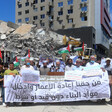 People hold banners and flags before a podium against a background of rubble