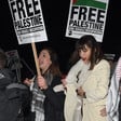 Two women stand beside each other, one holding a placard reading "Free Palestine" 