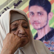 A woman rests her face on her fist with a poster of a man behind her 