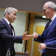 Two men in suits smile and gesture