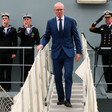 Simon Coveney walks on steps surrounded by three others in naval uniform 