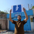 A man holds the Facebook logo upside down in front of the UNSCO building