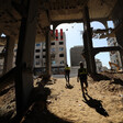 Two men stand on sand inside concrete skeleton of badly damaged building