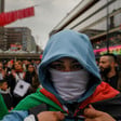 Close up of man in face mask and hoodie carrying Palestinian flag