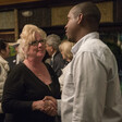 A man and a woman shake hands with people in background