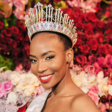 A woman wearing a crown and sash against a backdrop of flowers 