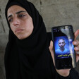 A woman holds up a phone with a picture of a man