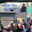 Soldier holding rifle stands behind elevated cinderblock above queue of Palestinians