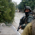 A soldier carrying a rifle looks at camera while standing on street