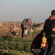 A protester in a wheelchair and another using crutches sit and stand near the Gaza-Israel boundary fence