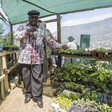 A man in hat surrounded by plants and mountains behind him