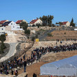 Landscape view shows hundreds of people walking along hillside with settlement homes in background