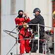 Man in handcuffs being removed by firefighters gives victory sign