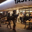 People stand in front of restaurant as Israeli soldiers walk along street