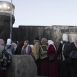 Women stand in front of concrete wall and military watchtower