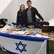 A woman and a man at a stall draped in an Israeli flag