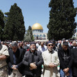 Men fold their arms while praying in front of mosque with gold dome