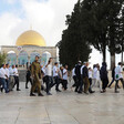 Men wearing religious accoutrements walk in front of the Dome of the Rock