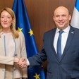 Woman and man shake hands and smile in front of EU and Israeli flags.
