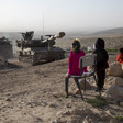 Children stand in front of tank on rocky hilltop