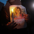 Close-up of pair of hands holding a candle and poster of Shireen Abu Akleh