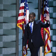 Man waves with American flags behind him