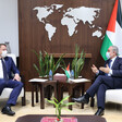 Two men wearing suits face each other while sitting in chairs with a table in between them