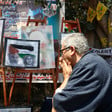 A man holds his hands to his face as he passes by posters of slain correspondent Shireen Abu Akleh