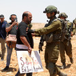 A man holding a sign is pushed by an Israeli soldier