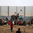 Crowd stands near militarized fence holding Palestine flags
