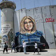 People walk past a mural of Shireen Abu Akleh wearing a press vest on Israel's militarized wall in the West Bank