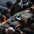 Men carry a flag-wrapped body on a stretcher with a weapon on top 