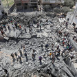 People stand atop the ruins of a destroyed building 