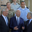 Three men in suits stand in front of military personnel