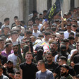 Men carry a body on a stretcher in a crowd that includes some with rifles 