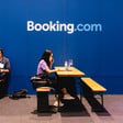Two people sit on benches and work in front of a Booking.com wall 