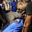 A woman touches shrouded body as others gather around
