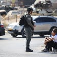 An Israeli soldier stands in front of two youths sitting on curb at checkpoint