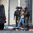 A young man grabs his wrist as an Israeli soldier holds him by his shoulder while two other soldiers hold rifles
